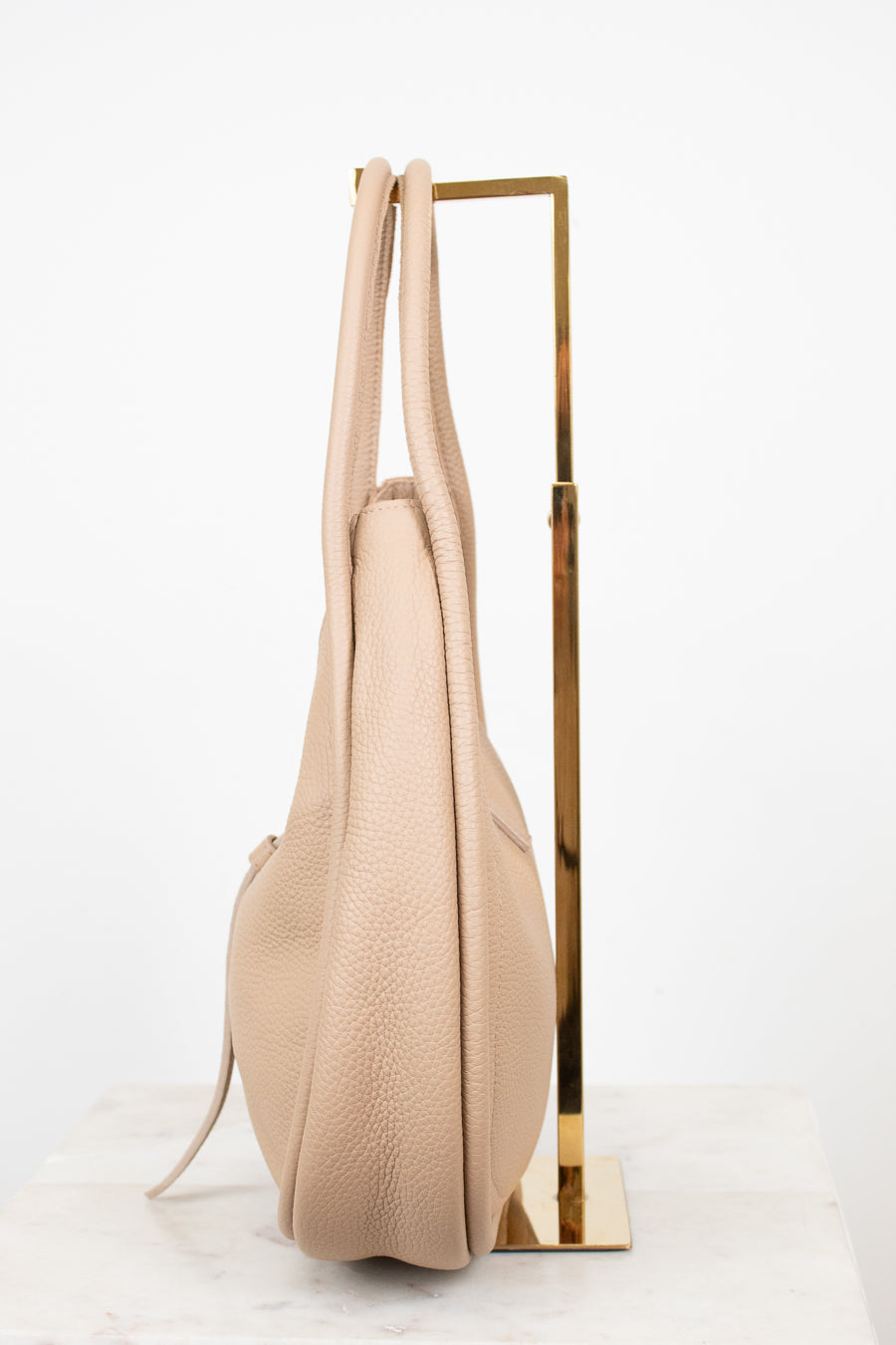 Beige handbag hanging on a gold stand against a white background