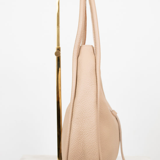Beige handbag on a gold stand against a white background