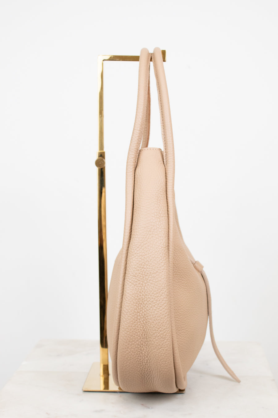 Beige handbag on a gold stand against a white background
