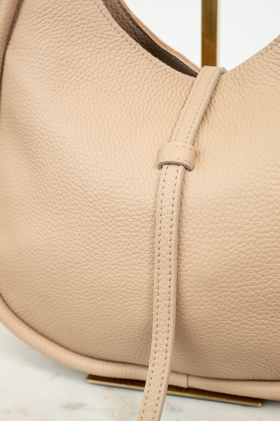 Close-up of a beige leather handbag with a strap on a light background