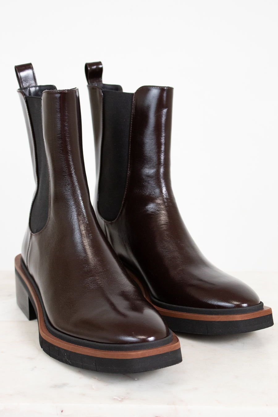 Pair of brown leather Chelsea boots with black elastic sides on a light background