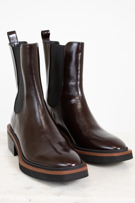 Pair of brown leather Chelsea boots with black elastic sides on a light background