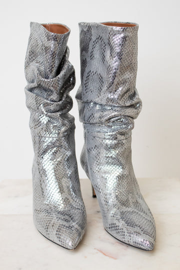 A pair of metallic silver snakeskin ankle boots with a slouchy draped design and pointed toes, set against a plain off-white background.