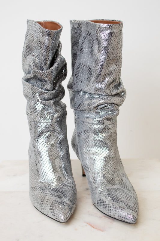 A pair of metallic silver snakeskin ankle boots with a slouchy draped design and pointed toes, set against a plain off-white background.