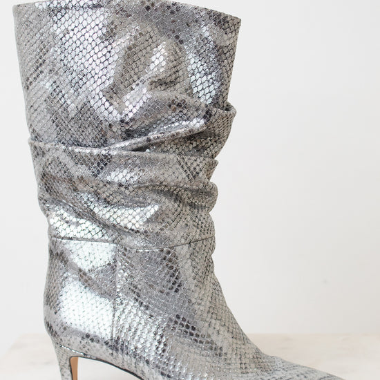A single metallic silver snakeskin slouchy boot with a pointed toe and a low kitten heel, shown against a plain off-white background.