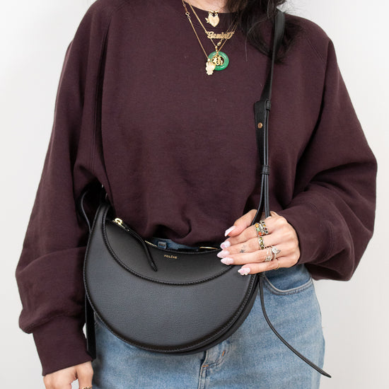 Person wearing a maroon sweatshirt and blue jeans, holding a black handbag against a white background