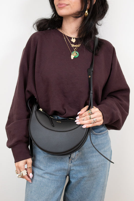 Person wearing a maroon sweatshirt and blue jeans, holding a black handbag against a white background