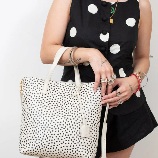 Woman holding a polka dot handbag against a plain background