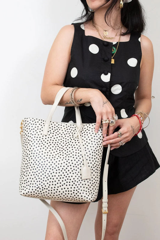 Woman holding a polka dot handbag against a plain background