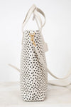White handbag with black polka dots and a gold clip on a white background