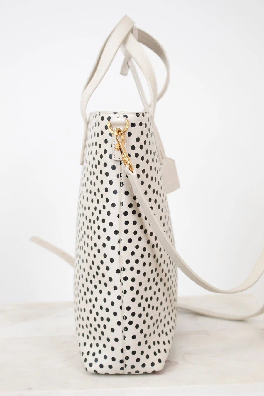 White handbag with black polka dots and a gold clip on a white background
