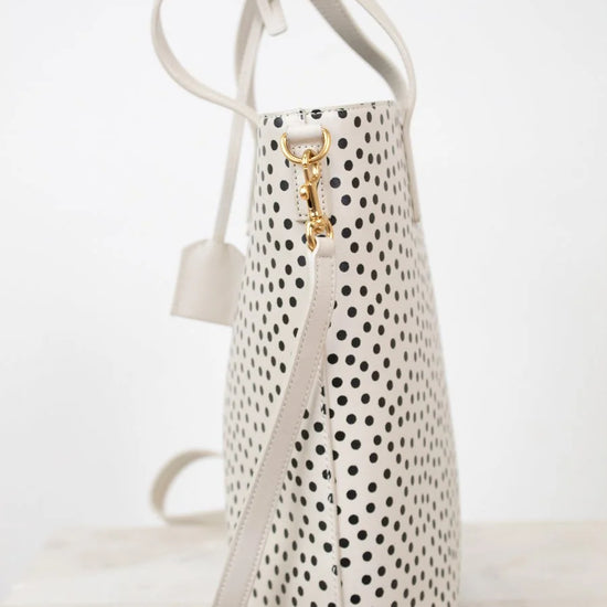 White handbag with black polka dot pattern and gold clasp on a white background