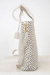 White handbag with black polka dot pattern and gold clasp on a white background