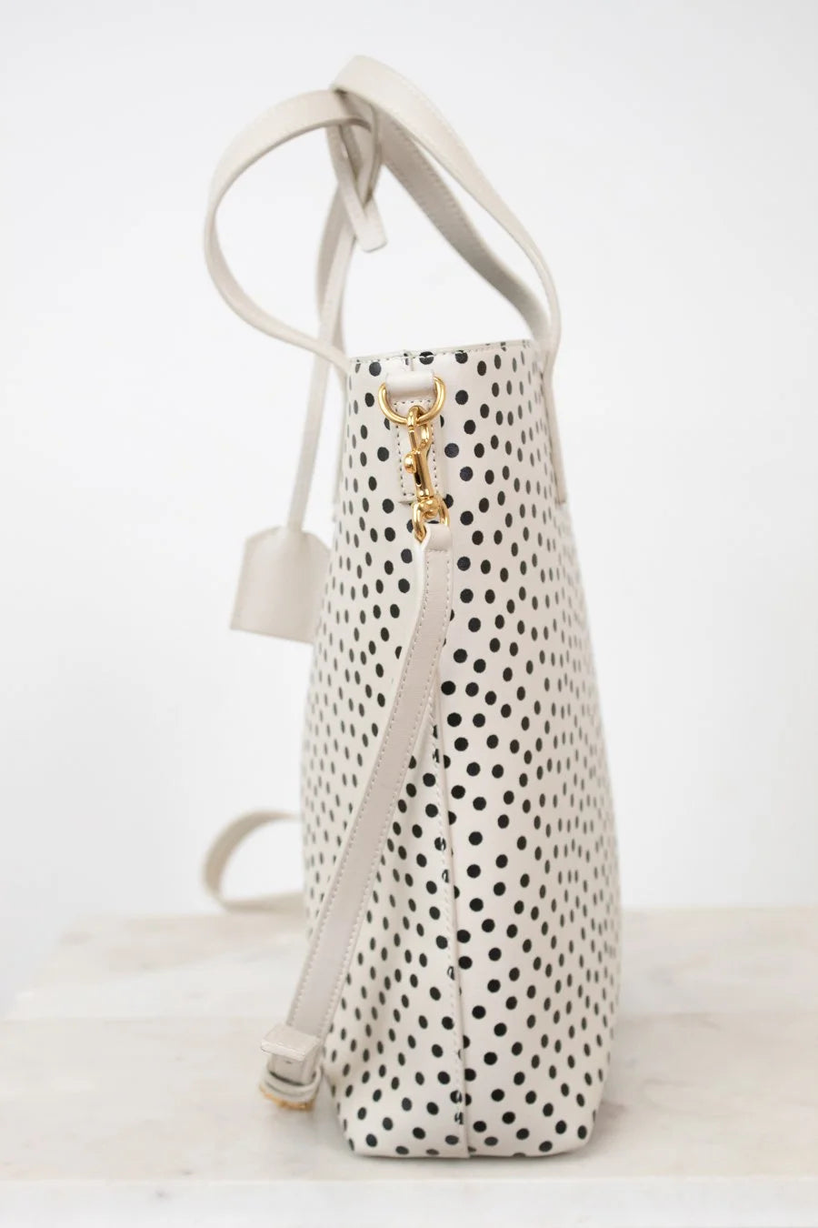 White handbag with black polka dot pattern and gold clasp on a white background