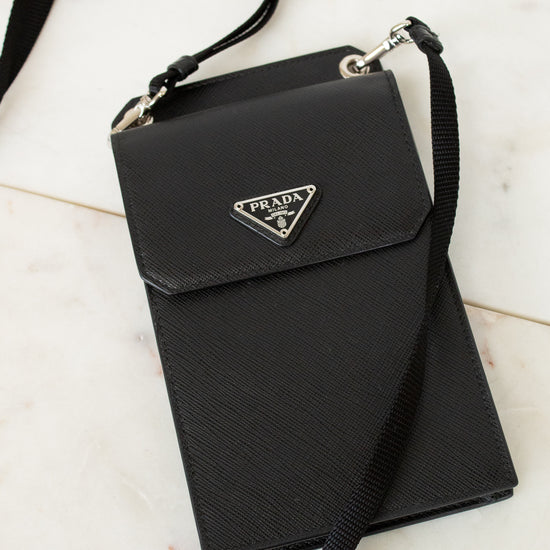 Black Prada handbag with a strap on a light marble background