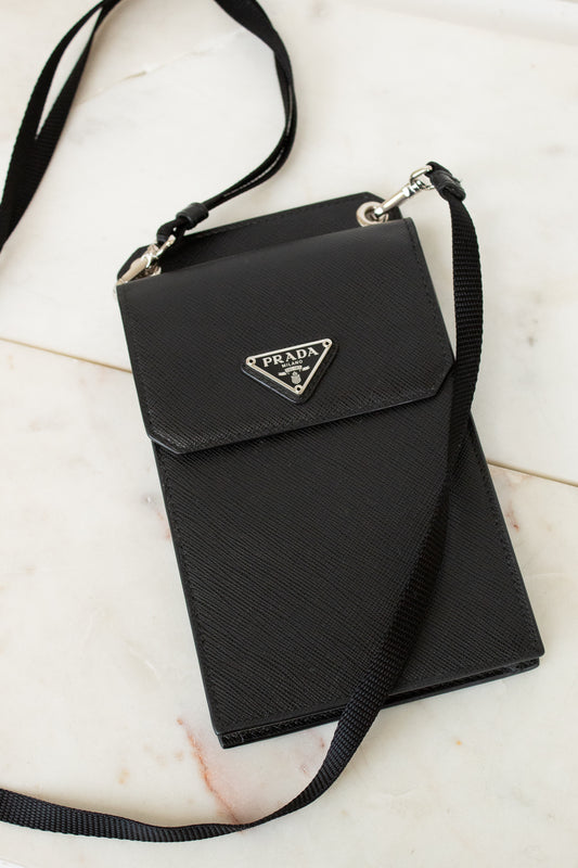 Black Prada handbag with a strap on a light marble background
