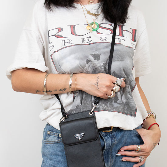 Person wearing a graphic t-shirt and jeans with a black Prada handbag.