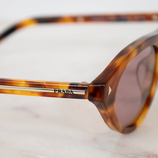 Tortoiseshell sunglasses with Prada logo on a marble surface