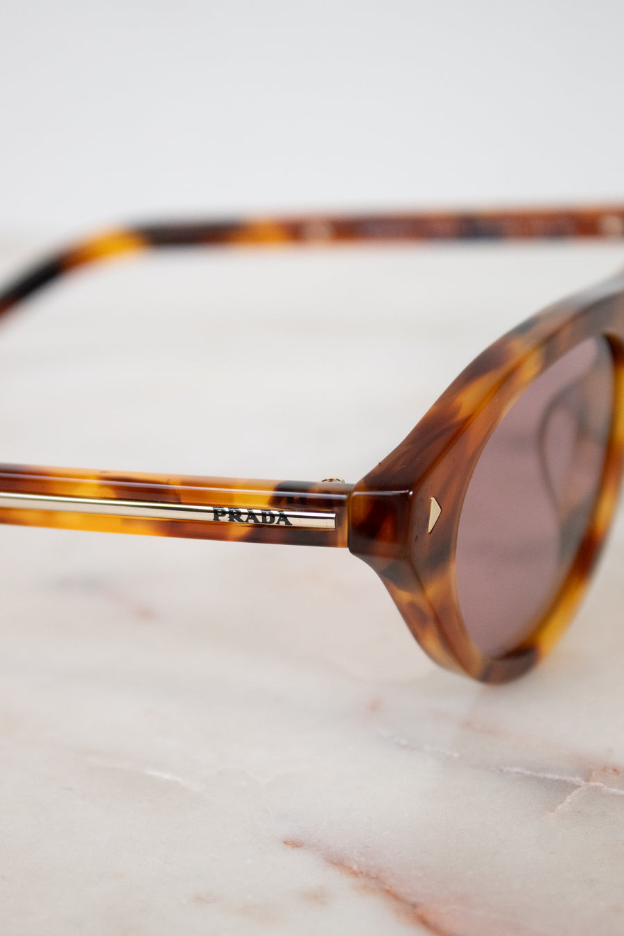 Tortoiseshell sunglasses with Prada logo on a marble surface