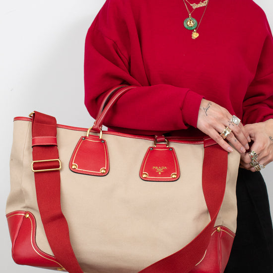 Person wearing a red sweater holding a beige and red handbag with 'Prada' branding.