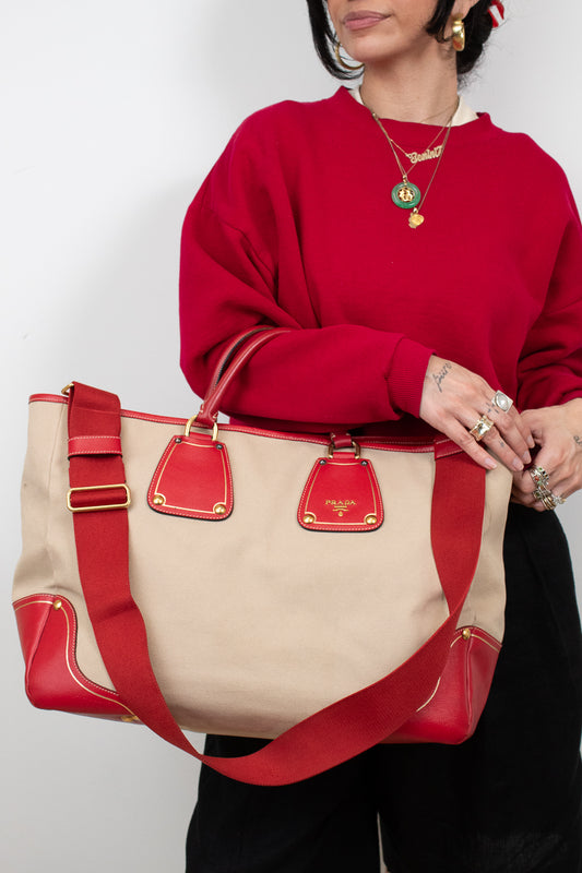 Person wearing a red sweater holding a beige and red handbag with 'Prada' branding.