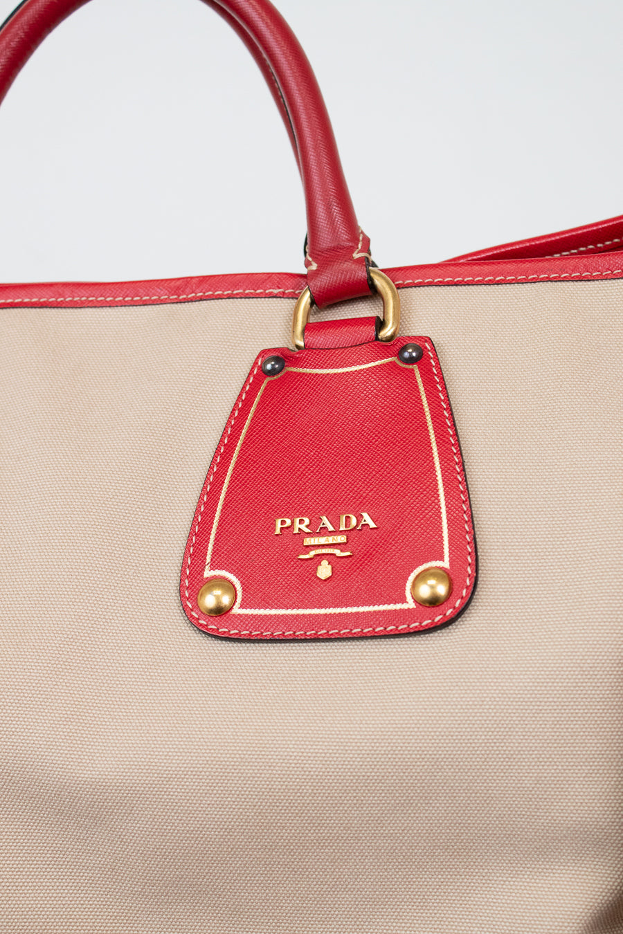 Beige handbag with red accents and Prada logo on a white background