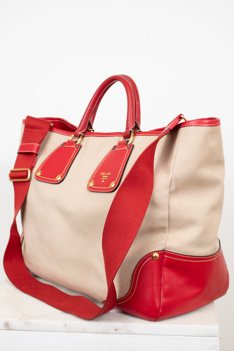 Beige and red handbag with gold accents on a white background