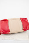 Red and beige clutch bag with gold studs on a white surface