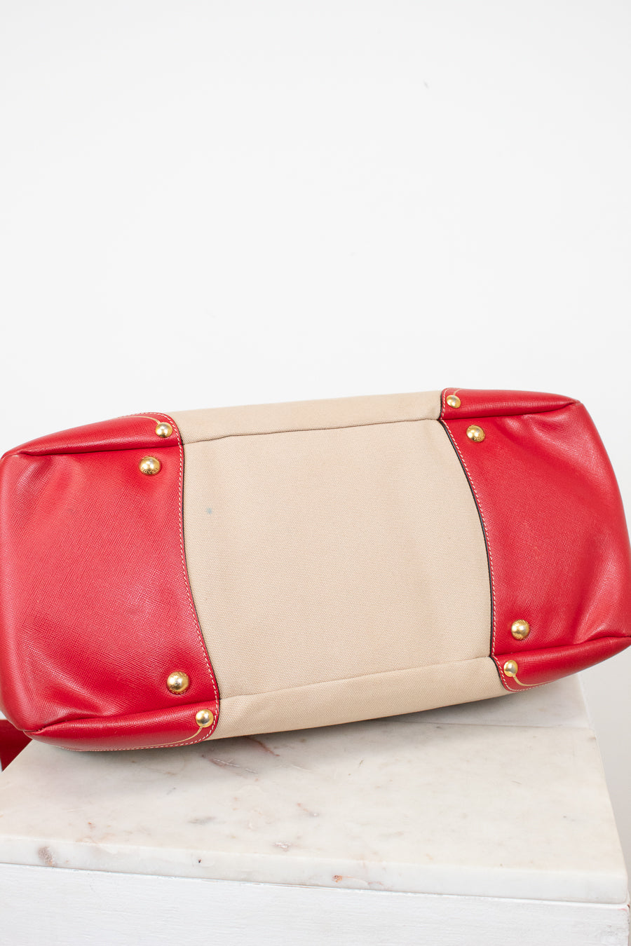 Red and beige clutch bag with gold studs on a white surface