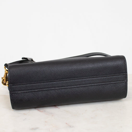 Bottom view of a black textured leather handbag  with gold-tone hardware, resting on a white marble surface against a white background.