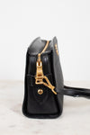 A close-up side view of a black leather handbag with gold-tone hardware, including a zipper pull, clasp, and a small gold logo on the front, set against a clean white background.
