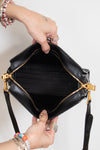 A black leather handbag with gold-tone hardware is held open by two hands against a plain white background.