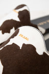 Close-up of a Prada slipper in brown and white cowhide with gold-tone 'PRADA' branding on the side, set against a neutral light background.