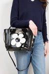 Person holding a black handbag with a white flower design on a plain background