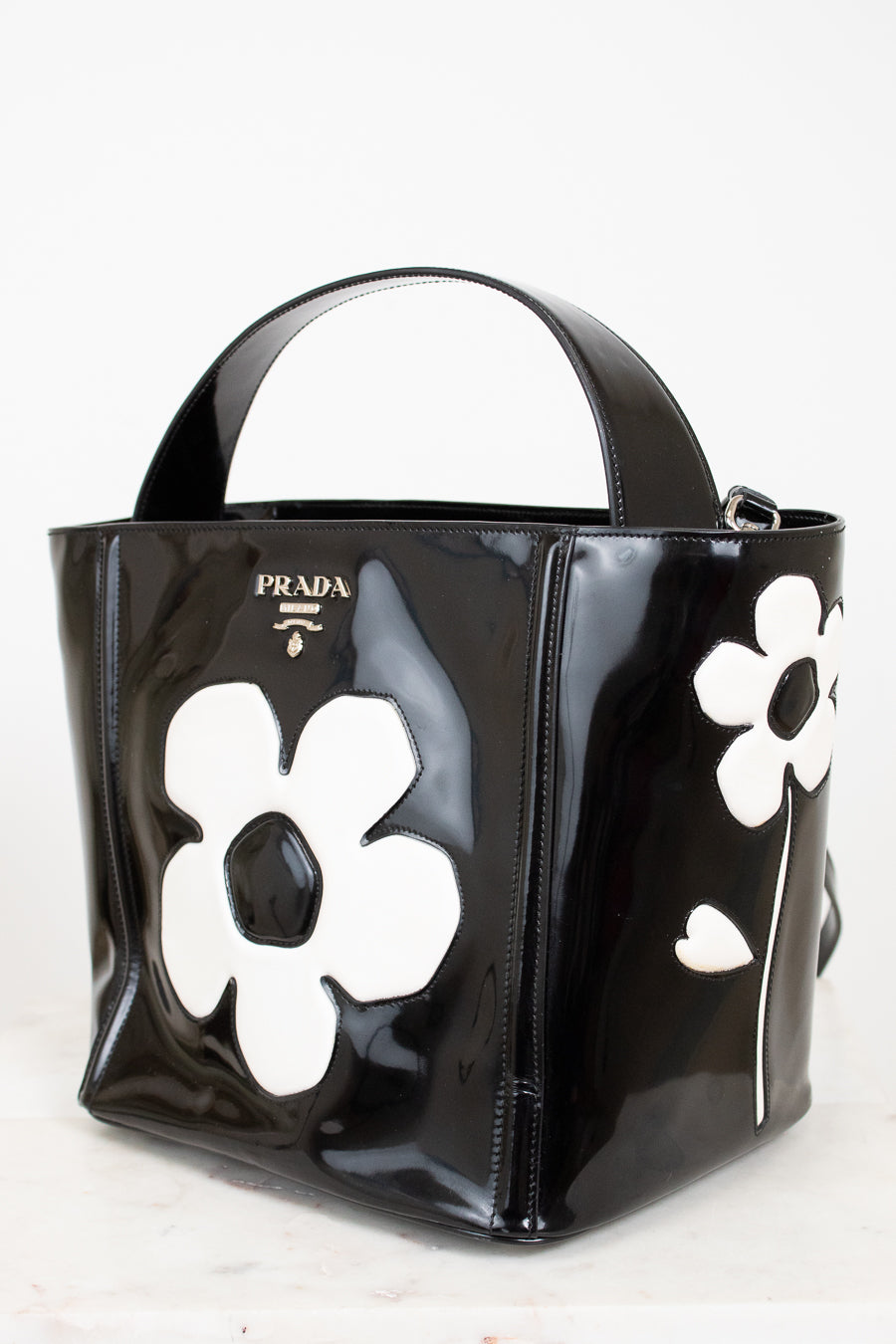 Black Prada handbag with white floral designs on a white background