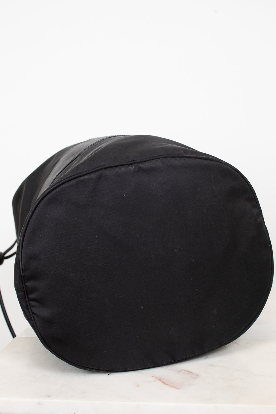 Bottom view of black nylon drawstring bucket bag displayed against a plain background