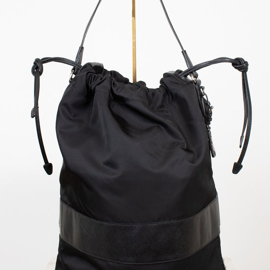 Back view of black nylon drawstring bucket bag displayed on a gold stand and against a plain background