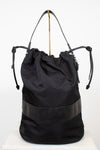 Back view of black nylon drawstring bucket bag displayed on a gold stand and against a plain background