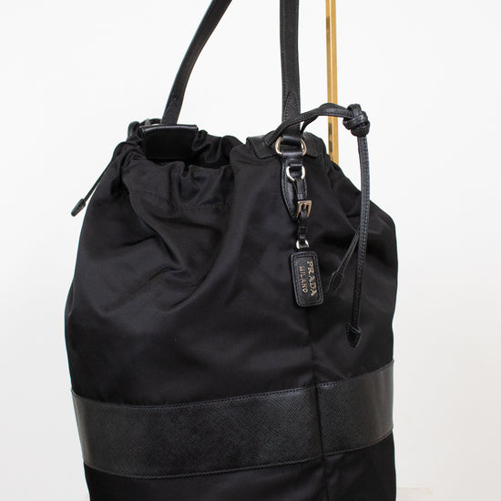 Black nylon drawstring bucket bag displayed on a gold stand and against a plain background