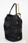 Black nylon drawstring bucket bag displayed on a gold stand and against a plain background
