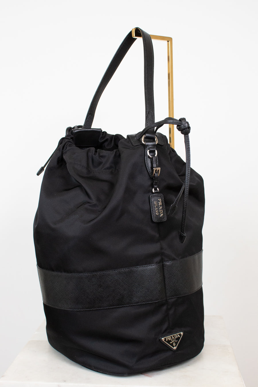 Black nylon drawstring bucket bag displayed on a gold stand and against a plain background