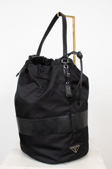 Black nylon drawstring bucket bag displayed on a gold stand and against a plain background