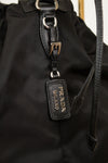 Close-up of 'Prada Milano' tag showing black leather and silver-tone details