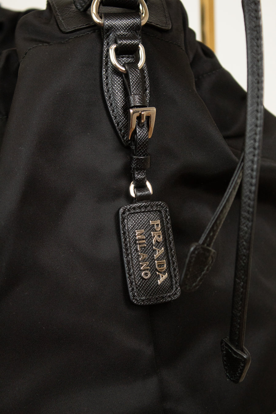 Close-up of 'Prada Milano' tag showing black leather and silver-tone details