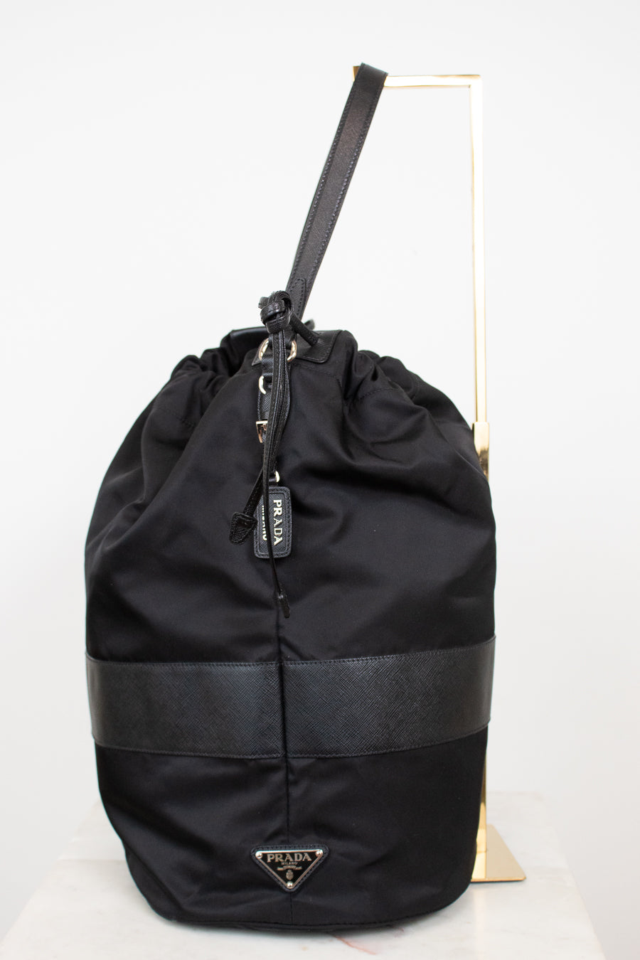 Side view of black nylon drawstring bucket bag displayed on a gold stand and against a plain background