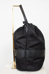 Side view of black nylon drawstring bucket bag displayed on a gold stand and against a plain background