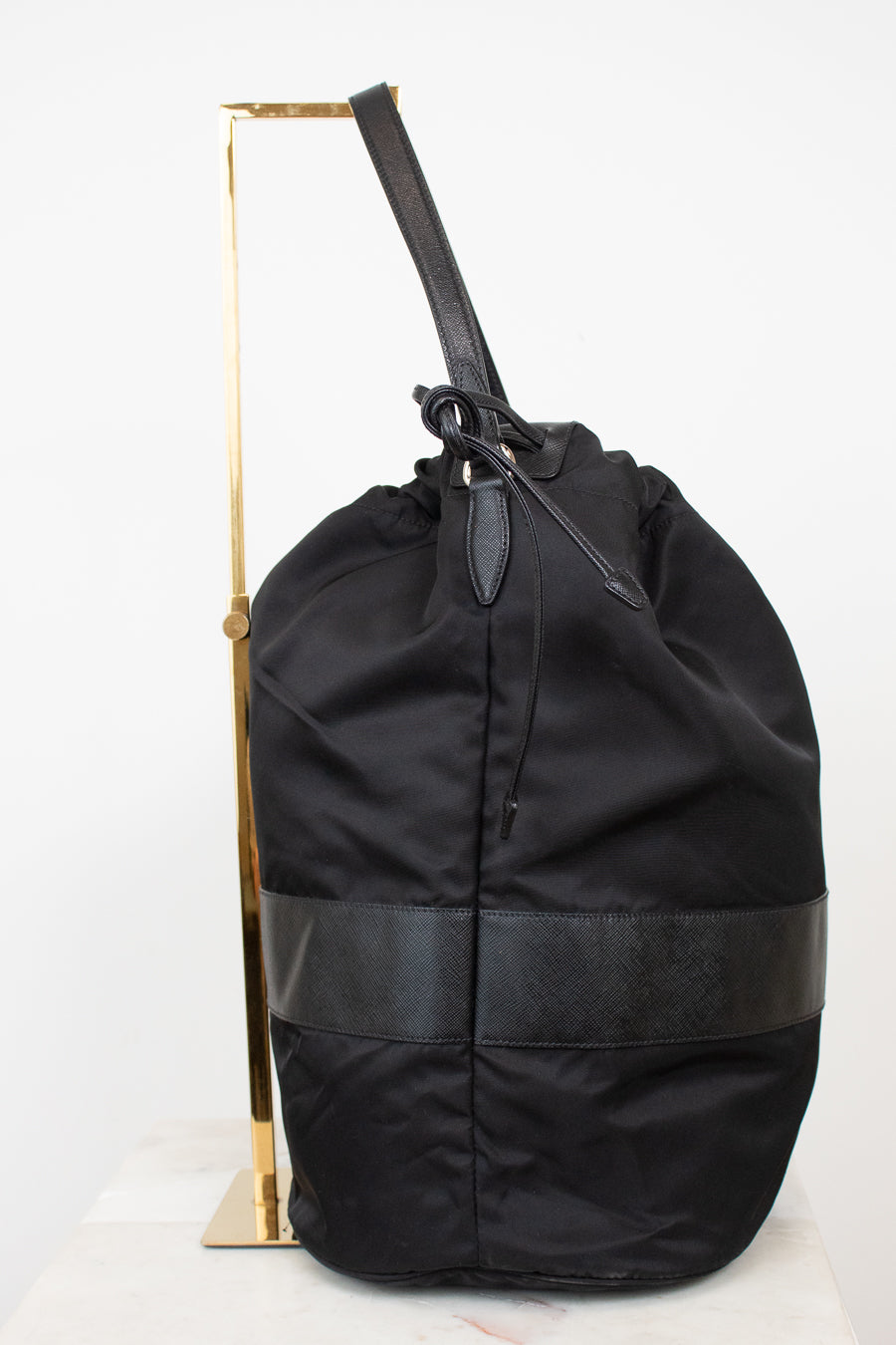 Side view of black nylon drawstring bucket bag displayed on a gold stand and against a plain background