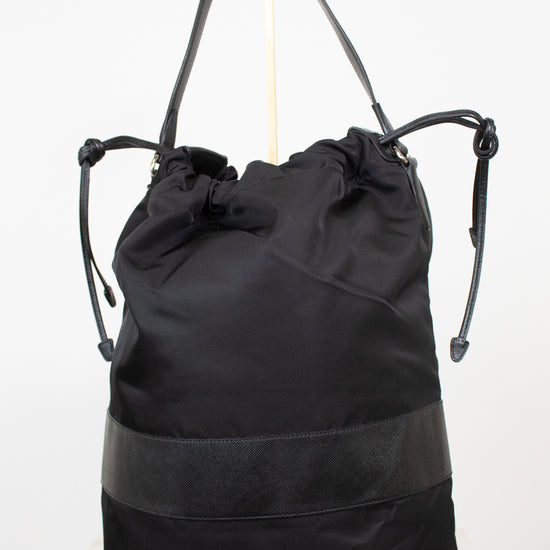 Back view of black nylon drawstring bucket bag displayed on a gold stand and against a plain background