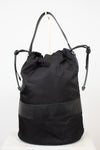 Back view of black nylon drawstring bucket bag displayed on a gold stand and against a plain background