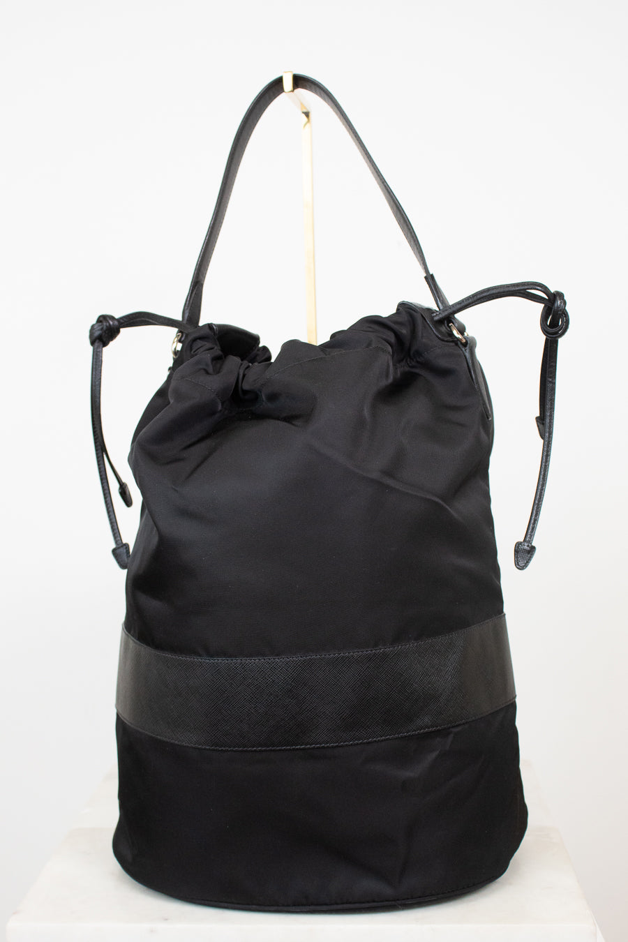 Back view of black nylon drawstring bucket bag displayed on a gold stand and against a plain background